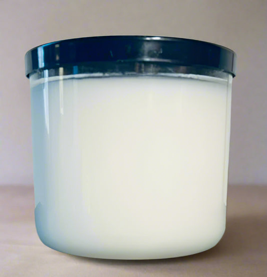 White candle in a glass jar with a black lid on a reflective surface.